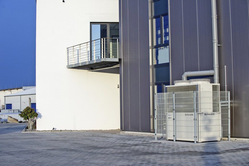 Die Gaswärmepumpe ist unauffällig hinter dem Gebäude installiert. Da die Mitarbeiterparkplätze direkt daneben liegen, wurde ein Schutzgitter angebracht.