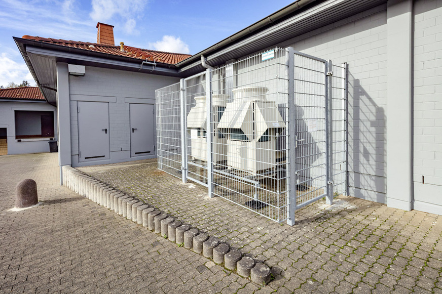 Die Außeneinheiten sind hinter einem Gitterschutz neben dem Gebäude aufgestellt und versorgen einen Kältekreis mit jeweils mehreren Innengeräten.