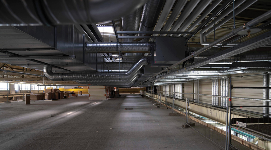 Zwischen dem Dach der Halle 8 mit integrierter Kranbahn und dem Dach der doppelstöckigen Büroräume verläuft eine der ersten ­semizentralen Lüftungsanlagen Europas mit knapp 300 Ventilatoren, verbaut in ­schallgedämpften Gehäusen.