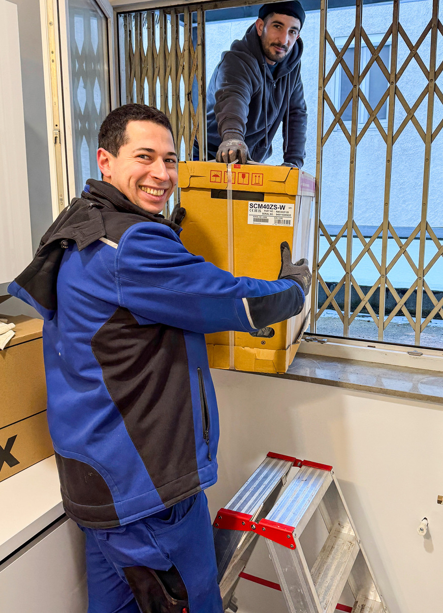 Das Fenstergitter hat nachgegeben. Philip Weber (links) und der Azubi Fettah Demier können die Außeneinheit endlich auf das Flachdach bringen.