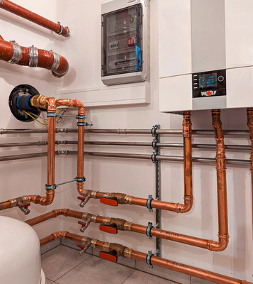 Bei der Elektroinstallation kann Zeit für die Montage und Abstimmung gespart werden, wenn eine Wärmepumpen-Unterverteilung von Wolf eingebaut wird. Links im Bild die Innenansicht der Wanddurchführung von Wolf und rechts die Inneneinheit der Wärmepumpe CHA von Wolf.