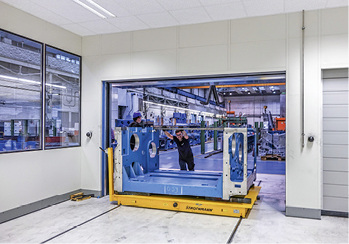 Dann werden sie auf einem Leichtlaufschienensystem, das für Gewichte bis zu 
8 t geeignet ist, in den Vortemperierraum gebracht. Dort werden sie 
24 Stunden lang bei 22 °C gelagert, bis die Teile ebenfalls diese 
Temperatur angenommen haben.

