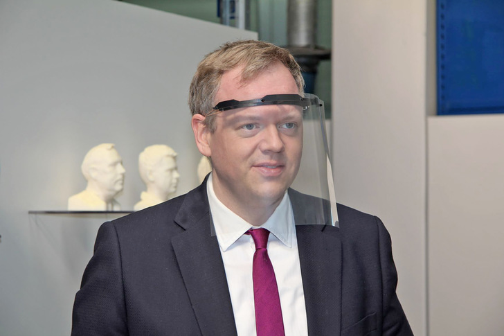 Landrat Dr. Matthias Neth (Hohenlohekreis) probiert einen Gesichtsschild aus, der aus einem gedruckten Träger, einer Tageslichtprojektorfolie und Gummiband besteht.