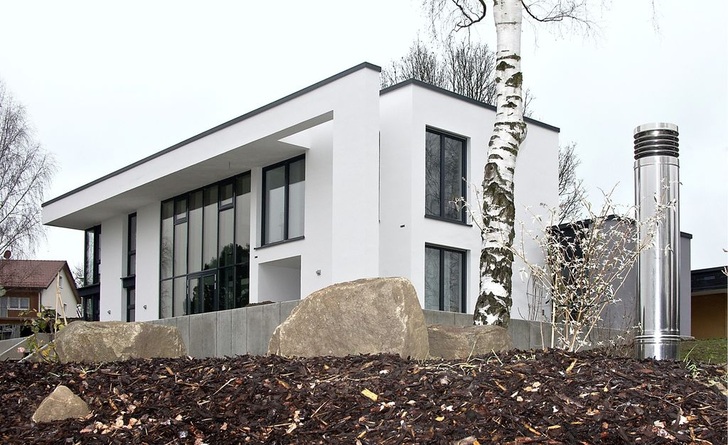 Das moderne Einfamilienhaus liegt am Ortsrand in Oberviechtach im Naturpark Oberpfälzer Wald. Eine Wärmepumpe und Lüftungsanlage von Dimplex ist in das nachhaltige Gesamtkonzept eingebunden. Rechts im Bild ist die Zuluft-Lamellenhaube des Erdwärmeübertragers zu sehen. Dieser wärmt die im Winter angesaugte Frischluft vor, indem er sie durch ein bis zu 50 Meter langes Rohrsystem im Erdreich leitet. Im Sommer ist das Prinzip umgekehrt: Die warme Außenluft wird durch das kühlere Erdreich abgekühlt.