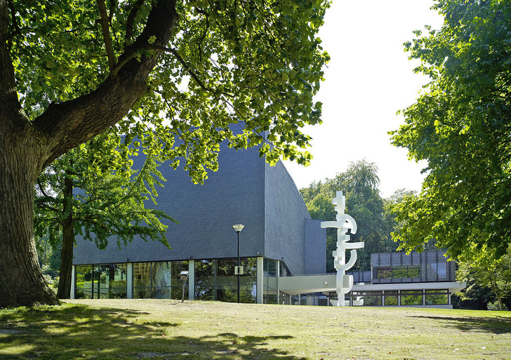 Das mit dunklem Schiefer verkleidete Konzerthaus der Hochschule für Musik in Detmold, das durch eine hochragende weiße Betonstele vor dem Eingangsportal gekennzeichnet ist, wurde nach über 40-jähriger Nutzung einer Kernsanierung unterzogen.