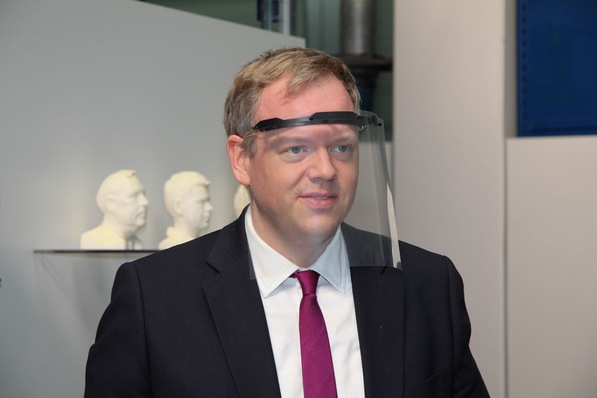 Landrat Dr. Matthias Neth (Hohenlohekreis) probiert einen Gesichtsschild aus, der aus einem gedruckten Träger, einer Tageslichtprojektorfolie und Gummiband besteht.